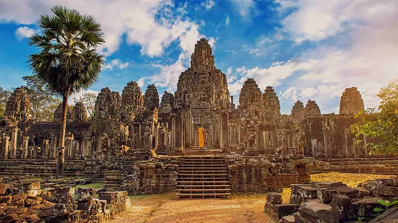 Las torres del templo Bayon, en Angkor Thom, con una palmera y un monje de túnica naranja en la entrada