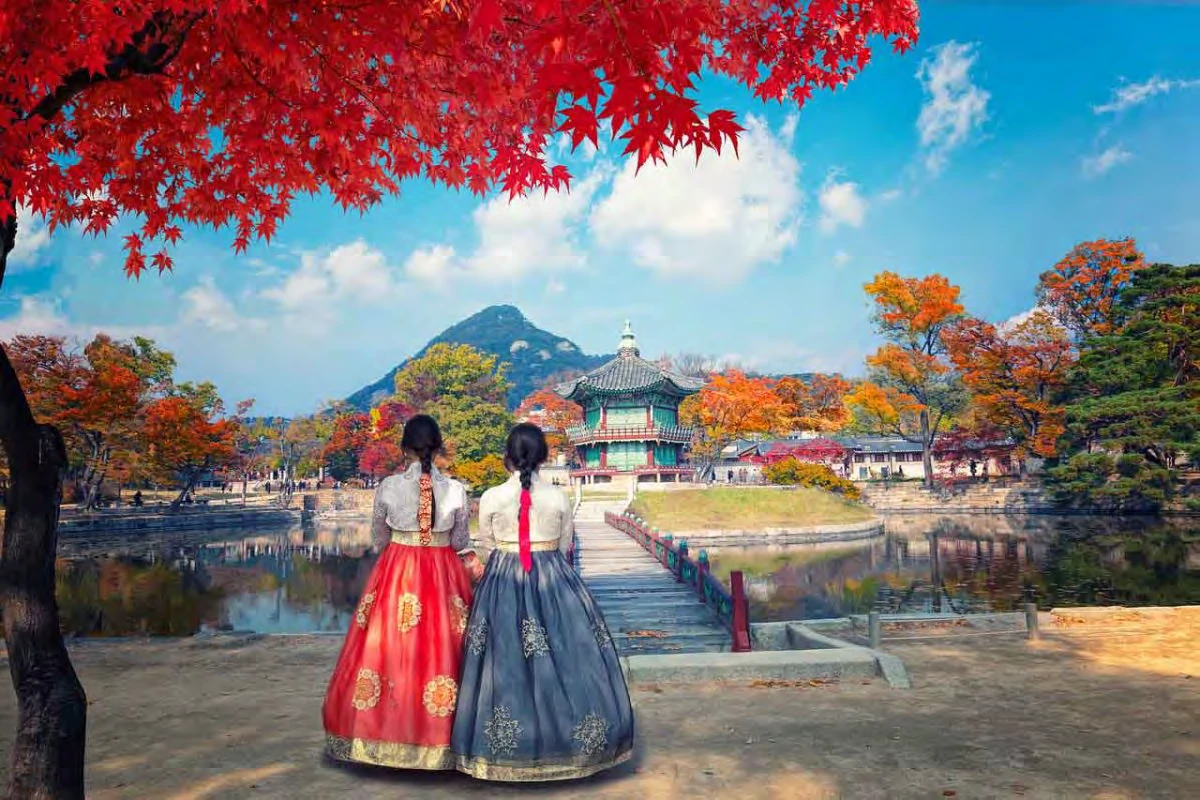Dos mujeres vestidas con hanbok frente al pabellón Hyangwonjeong, en el palacio Gyeongbokgung, en otoño