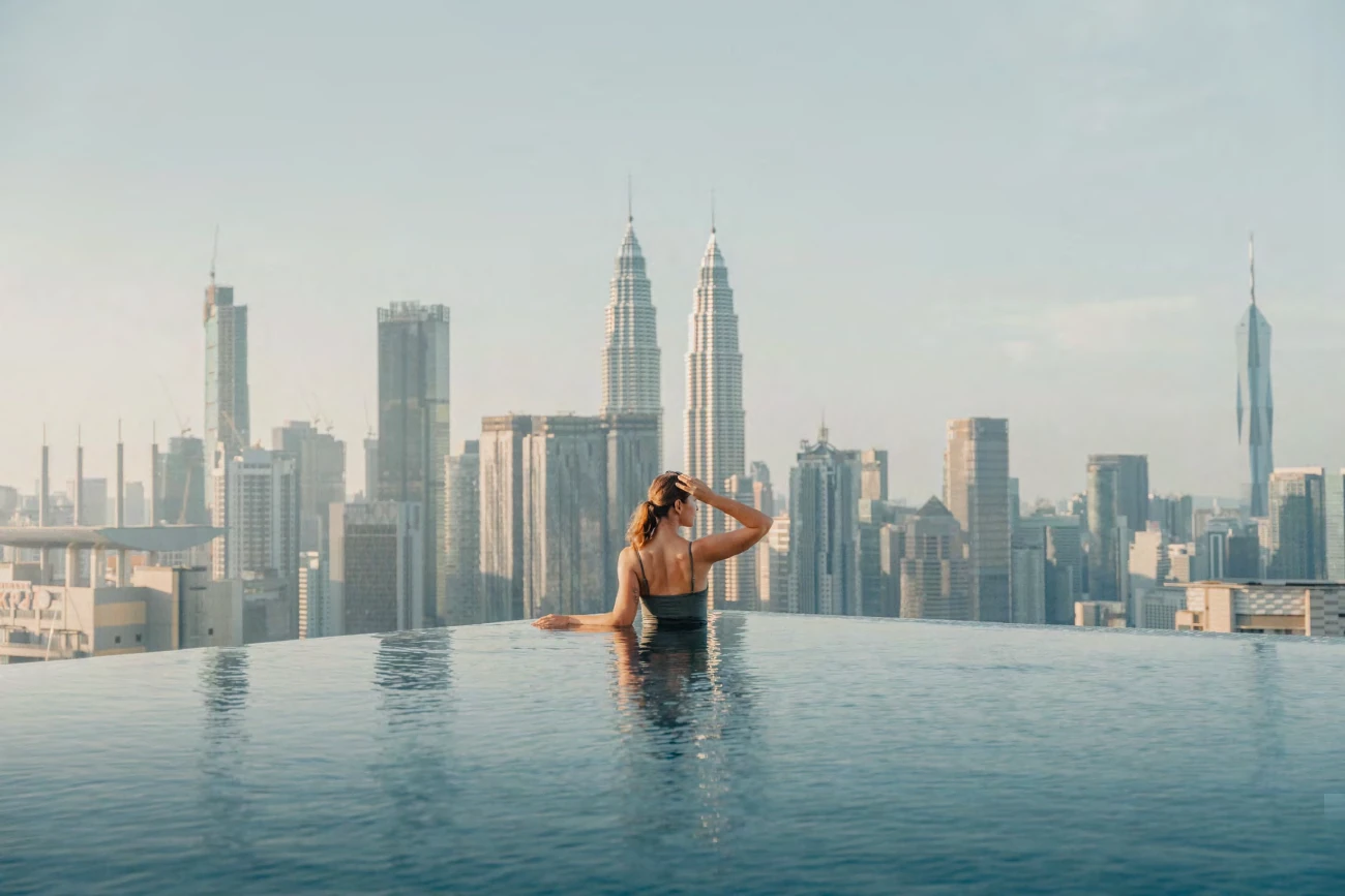 Una viajera en una piscina en altura frente a las torres Petronas y los rascacielos de Kuala Lumpur