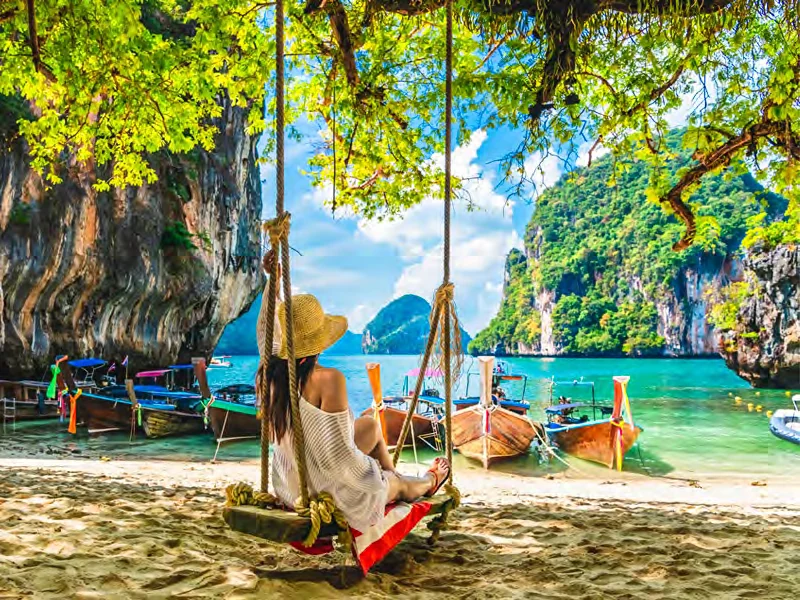 Viajera en una hamaca frente a una playa con botes de cola larga en Krabi