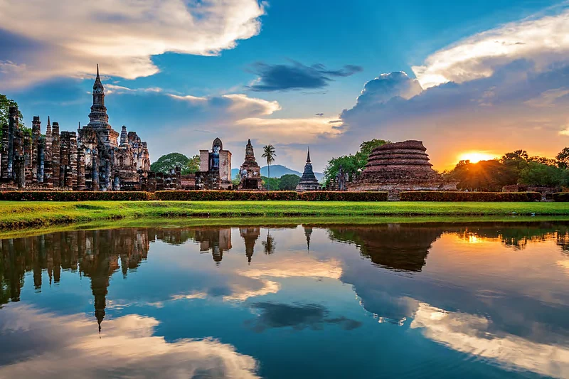 Ruinas de templos del parque histórico de Sukhothai reflejadas en un estanque al atardecer