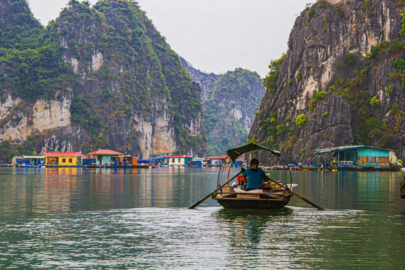 Una barca a remo frente a un pueblo flotante entre los islotes de piedra caliza de la bahía de Halong